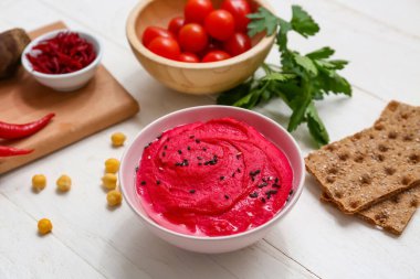 Bir kase lezzetli pancar humusu, domates, maydanoz ve beyaz ahşap arka planda krakerler.