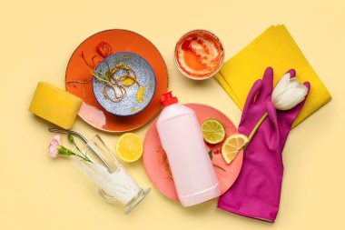 Sarı arka planda plastik eldiven, çiçek ve deterjan olan bir sürü kirli tabak.