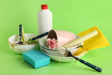Yeşil arka planda deterjanı, süngeri ve bezi olan bir sürü kirli bulaşık.