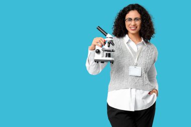 Mavi arka planda mikroskobu olan Afro-Amerikan bayan öğretmen.