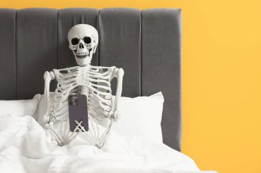 Yatağında cep telefonu olan insan iskeleti.