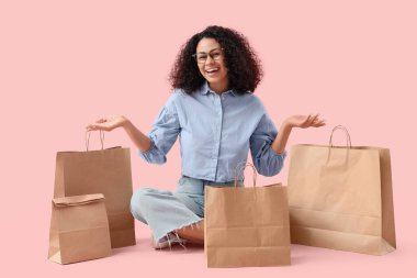 Pembe arka planda oturan, kağıt torbalı genç Afro-Amerikalı kadın. Yemek dağıtım servisi.