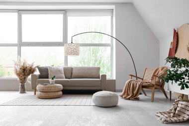 Şık oturma odasının içinde rahat gri kanepe, puf ve otlar var.