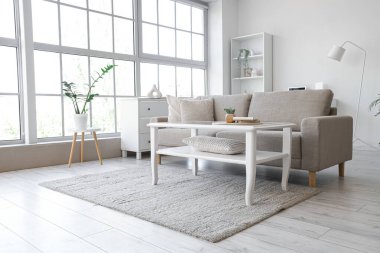 Oturma odasının içinde yumuşak kanepe, masa ve pencere var.