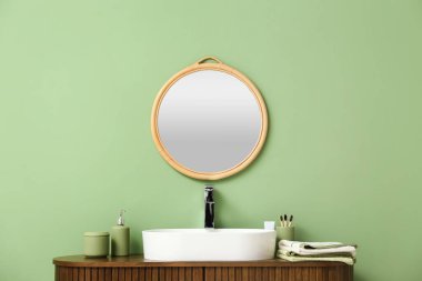 Banyoda lavabosu olan ahşap dolabın üzerindeki yeşil duvarda asılı şık ayna.