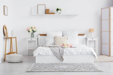 Şık bir yatak odası, rahat bir yatak ve güzel şakayıklar.