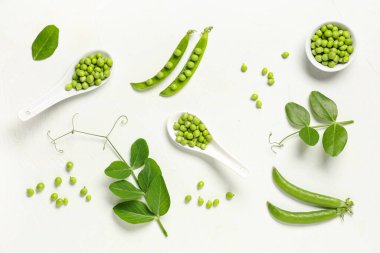 Beyaz arka planda taze bezelyeler ve kaşıklar.