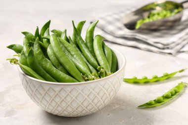 Gri arkaplanda yeşil bezelye kabukları olan kase, yakın plan