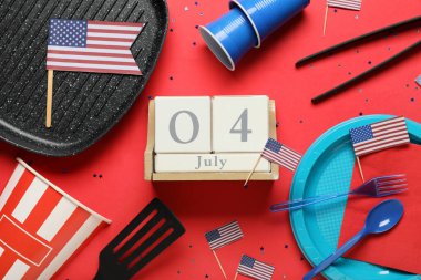 ABD bayrakları, 4 Temmuz tarihli takvim, kırmızı arka planda plastik yemek takımı ve barbekü aletleri. Bağımsızlık Günü kutlamaları
