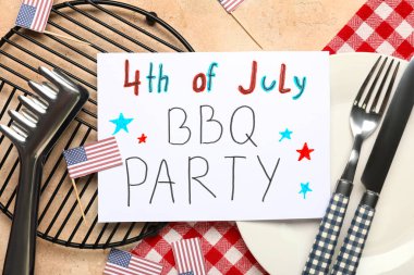 ABD bayrakları, 4 Temmuz barbekü partisi yazılı tebrik kartı, bej grunge arka planda yemek takımı ve barbekü maşası. Bağımsızlık Günü kutlamaları