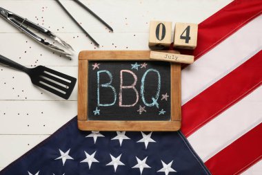 Amerikan bayrağı, mangal tahtası, 4 Temmuz tarihli takvim ve beyaz ahşap arka planda barbekü aletleri. Bağımsızlık Günü kutlamaları