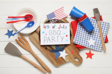 ABD bayrağı, 4 Temmuz barbekü partisi ve beyaz ahşap arka planda barbekü aletleri yazılı tebrik kartı. Bağımsızlık Günü kutlamaları