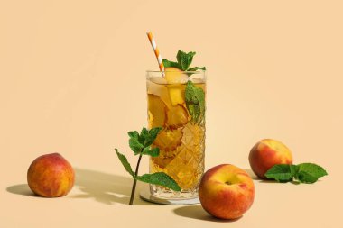 Bej arkaplanda nane ve şeftalili bir bardak lezzetli buzlu çay.