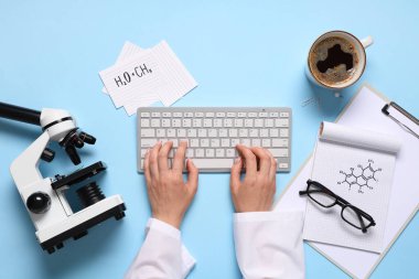 Klavyesi, modern mikroskobu ve mavi arka planda bir fincan kahvesi olan kadın bilim adamının elleri.