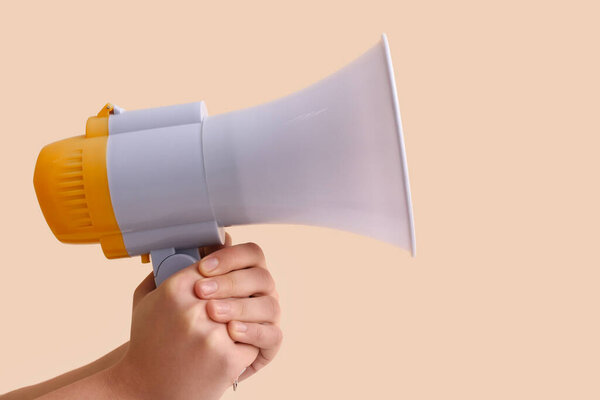 Женские руки с мегафоном на бежевом фоне