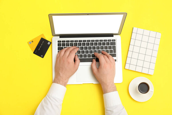 Мужские руки с ноутбуком, кредитные карты и чашку кофе на желтом фоне