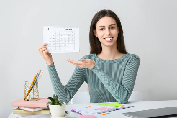 Красивая молодая счастливая женщина указывает на календарь в офисе