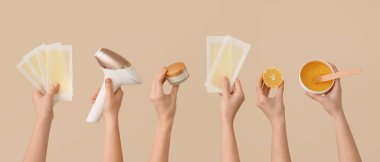 Ellerinde fotoepilatör, balmumu şeritleri, krema ve bej arka planda şekerleme macunu olan eller. 