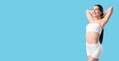 Açık mavi arka planda iç çamaşırlı mutlu genç bir kadın. 