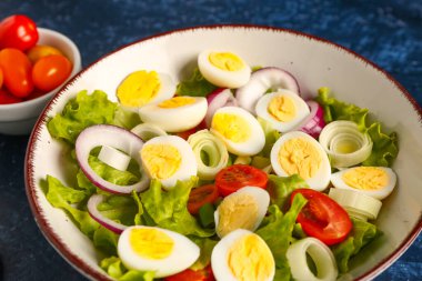 Bıldırcın yumurtalı, domatesli, soğanlı ve lacivert arkaplanlı lezzetli salata. Yakın plan.