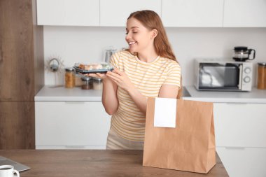 Mutfakta suşi ve kese kağıdıyla mutlu genç bir kadın.