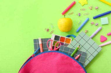 Taze elmalı sırt çantası ve yeşil arka planda farklı kırtasiye malzemesi.