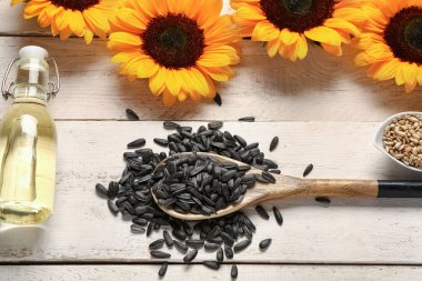 Ayçiçekleri, tohumlu kaşık ve hafif ahşap arka planda bir şişe yağ.