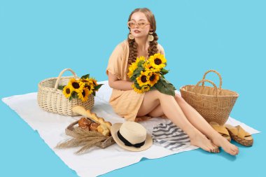 Güzel ayçiçekleri olan genç bir kadın mavi arka planda piknik yapıyor.