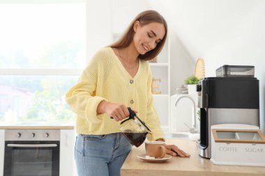 Genç ve güzel bir kadın mutfaktaki espresso bardağına dolduruyor.
