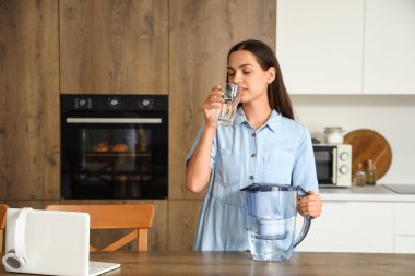 Mutfakta filtre sürahi su içen güzel genç bir kadın.