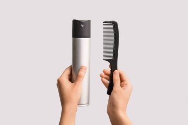 Beyaz arka planda saç spreyi ve saç fırçası olan kadın elleri..