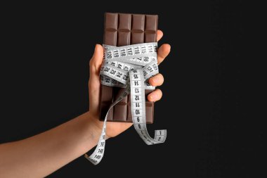 Çikolatalı kadın eli ve siyah arka planda mezura.