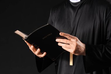 Genç rahip siyah arka planda İncil okuyor, yakın plan.