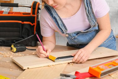 Dişi marangoz, atölyede kare cetvelle kalas genişliğini ölçüyor, yakın plan.