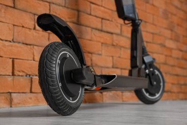 Siyah modern elektrikli scooter, tuğla duvarın yanında.
