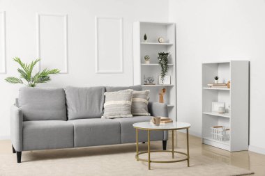 Gri kanepe, masa ve raf üniteleriyle aydınlık oturma odasının içinde.