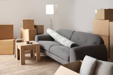 Cardboard boxes with black sofa, rolled carpet and table in living room on moving day