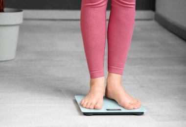 Evde terazinin üzerinde duran genç bir kadın. Kilo verme konsepti