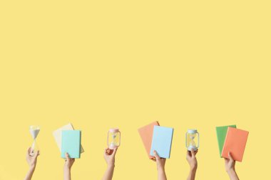 Kum saati tutan kadın eller ve sarı arka planda kitaplar.