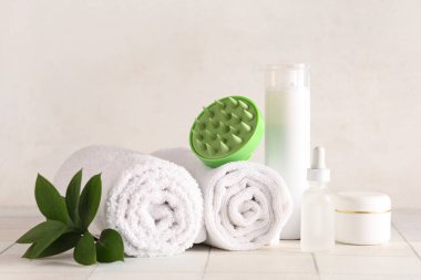 Farklı kozmetik ürünleri ve beyaz fayans masasında havluları olan saç derisi masaj aleti.