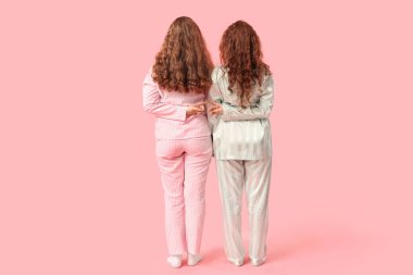 Pembe arka planda pijamalı mutlu kızıl kız kardeşler.