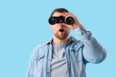 Mavi arka planda dürbünle bakan genç adam şaşırdı.