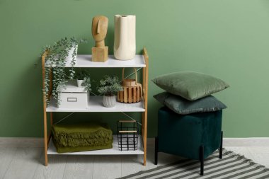 Yeşil duvarın yanında dekoru ve pouf olan modern raf ünitesi.