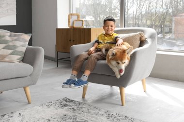 Küçük mutlu Asyalı çocuk ve şirin Corgi köpeği evdeki koltukta oturuyor.