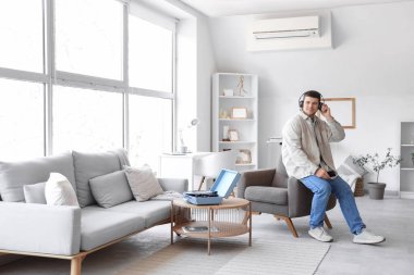 Kulaklıklı, cep telefonlu genç sakallı adam evde müzik dinliyor.