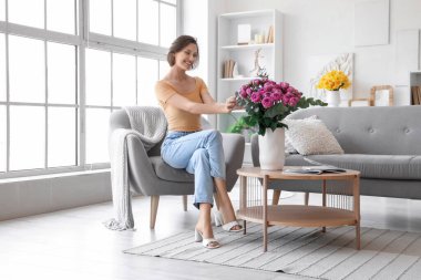 Evdeki koltukta pembe gülleri olan genç bir kadın oturuyor.