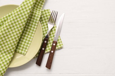 Tabak, çatal bıçak takımı ve bej ahşap arka planda kareli peçeteler.