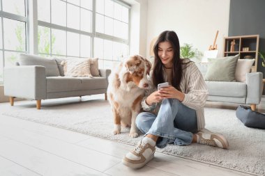 Evde cep telefonu kullanan Avustralyalı çoban köpeği olan genç bir kadın.