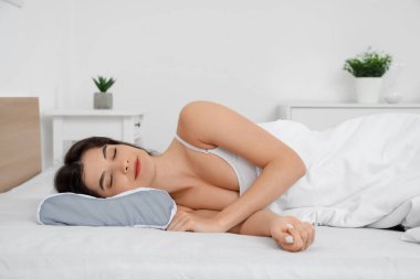 Pijamalı genç bir kadın evdeki beyaz yatakta yumuşak ortopedik yastıkta uyuyor.