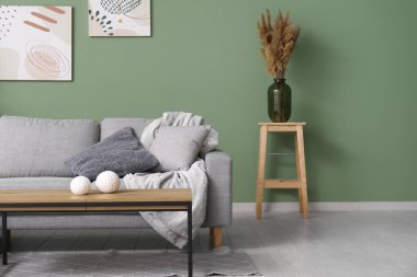 Gri kanepesi, sehpası ve yeşil duvarlı resimleri olan şık bir oturma odası.